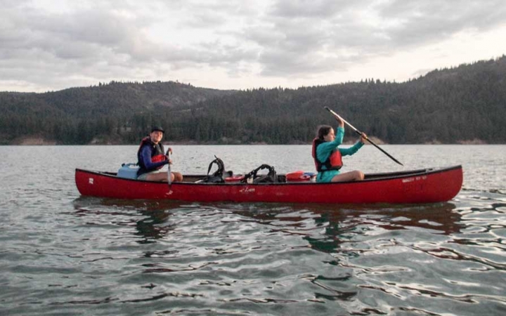two girls paddle a red canoe on still water
